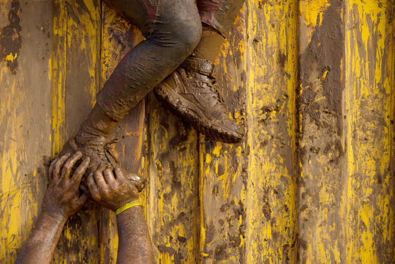 two-mud-runners-helping-eachother-over-obstacle